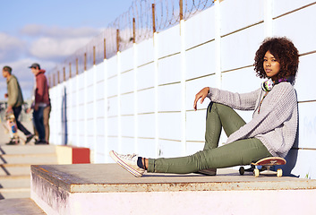 Image showing Portrait, serious and woman with skateboard in city by wall in summer for sport, fashion or relax outdoor. Young person, skate park and gen z girl in casual clothes with headphones in South Africa