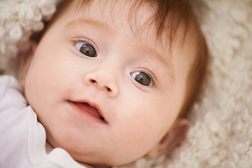 Image showing Happy, cute and closeup of baby on blanket playing for child development and curious face. Smile, sweet and young girl kid, infant or newborn relaxing and laying on bed in nursery room at home.