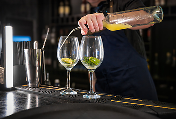 Image showing Bartender pouring a mixed drink into two elegant glasses