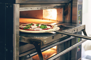 Image showing Close-up of a hand placing an uncooked pizza