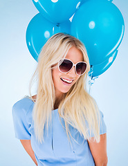 Image showing Woman, balloons and smile in studio with sunglasses for event, party or celebration by blue background. Girl, person or model with glasses, happy and excited with fashion, trendy style or birthday