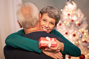 Image showing Christmas, portrait and gift with senior couple with love, care and support together in a home on holiday. Tree, retirement and marriage with a smile and hug in a house with celebration and present