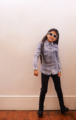 Image showing Girl, child and fashion or sunglasses for style and looking cool on a wall background at home. Happy portrait of a kid or child with trendy clothes, casual and accessory or shades for fun indoors