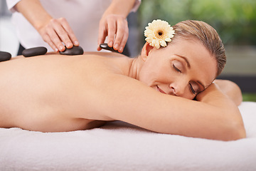 Image showing Woman, hands and hot stone massage with masseuse at spa, flower for natural treatment and wellness with zen. Calm, peace and luxury bodycare with warm rocks for detox, self care and holistic healing