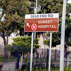 Image showing City, outdoor and information with road, signage and text with icon for hospital and symbol with nature and urban town. Street, direction to a medical facility and outdoor with fence, board and tree