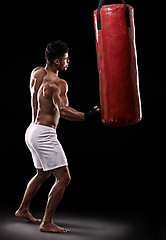 Image showing Practice, boxer and man with punching bag in studio with gloves for training with strength and muscle. Adult, athlete and male person in dark background, healthy and power with body, job and sport