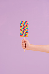 Image showing Hand, lollipop and candy in studio for dessert sweets on purple background for carnival snack, hungry or mockup space. Fingers, stick and treats for party food or sugar eating, birthday or unhealthy