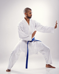 Image showing Studio, karate and black man with martial arts, training and blue belt for instructor in white background. Discipline, male person and adult with technique for health, goju ryu and movement for power