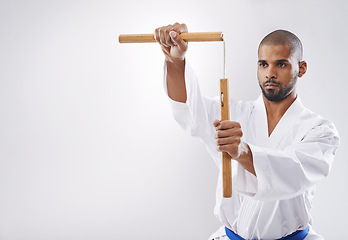 Image showing Nunchucks, karate and man in martial arts fight with weapon in training for defence in white background of studio. Nunchaku, exercise and fighting with equipment in sport with skill and power in club