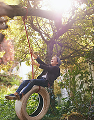 Image showing Boy, child and playing on tyre swing in garden with happiness, recreation or countryside vacation in summer. Kid, excited and diy adventure playground in backyard with sunlight and trees in nature