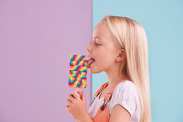 Image showing Studio, girl and lick with lollipop, dessert and choice for snack and childhood. Child, sweets and yummy candy for tasty, eating and happy or excited on vibrant split pastel pink and blue background