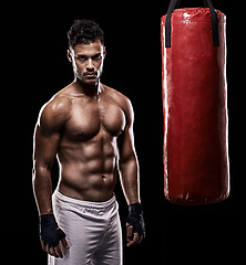 Image showing Serious, boxer and portrait of man, punching bag and gloves for training with strength and muscle. Adult, athlete and male person in dark background, healthy and power with body, sport and studio