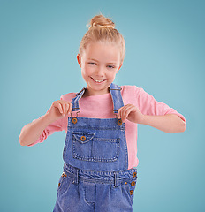 Image showing Child, portrait and smile in studio with confidence in dungarees on blue background, fashion or mockup space. Girl, school student and positive childhood in Australia with good mood, growth or kid