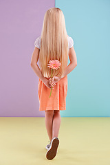 Image showing Fashion, flower and back of child in studio with cute, trendy and casual dress for outfit. Sweet, gift and young girl kid with blonde hair, style and pink floral plant by color block background.