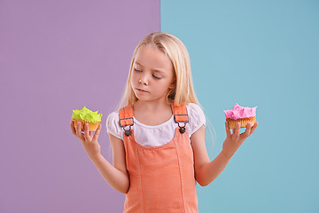 Image showing Studio, girl and choice with cupcakes, dessert and decision for snack and childhood. Child, sweets and yummy selection for tasty, eating and choosing on vibrant split pastel pink and blue background