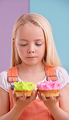 Image showing Studio, girl and decision with cupcakes, desert and choice for snack and childhood. Child, sweets and yummy selection for tasty, eating and choosing on vibrant split pastel pink and blue background