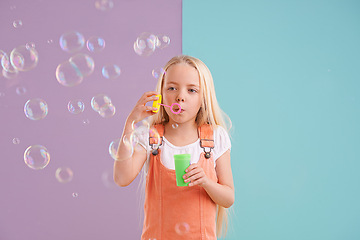 Image showing Child, blowing bubbles and playing in studio as holiday activity for leisure, childhood development or mockup space. Female person, kid and toy or split purple with blue background, innocent or fun