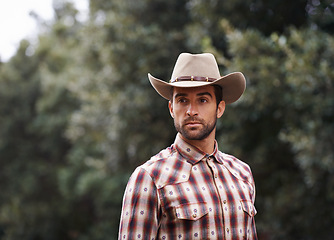 Image showing Man, hat and outdoor cowboy fashion, western culture and countryside ranch in Texas. Male person, accessory and flannel shirt for farmer aesthetic, nature and plaid style by trees or outside bush