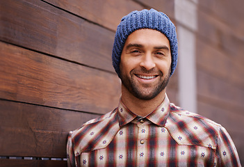 Image showing Portrait, smile and man on wood wall background outdoor in casual clothes, outfit or apparel. Face, happy and stylish person in beanie, shirt and trendy fashion for profile picture with hat in Spain