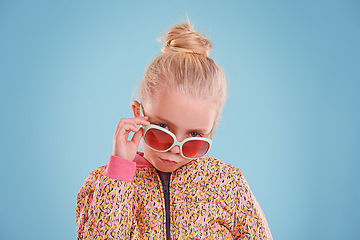 Image showing Portrait, fashion and child with sunglasses in studio with trendy, cool and funky outfit with confidence. Stylish, pout and girl kid model with cool style and accessory isolated by blue background.