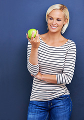 Image showing Woman, smile and apple in studio for healthy diet on blue background or fruit nutrition, snack or fibre. Female person, relax and wellness eating with mockup space or vegan detox, food or lose weight