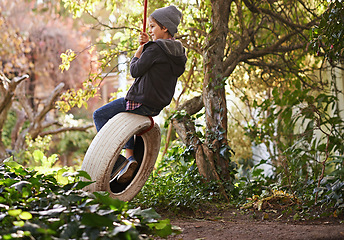 Image showing Boy, tyre swing and playing in garden with happiness, recreation and countryside vacation in summer. Child, smile and diy adventure playground in backyard of home with sunshine and trees in nature