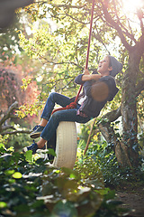 Image showing Boy, child and playing on tyre swing in garden with happiness, recreation and countryside vacation in summer. Kid, excited and diy adventure playground in backyard of home with sunlight and trees