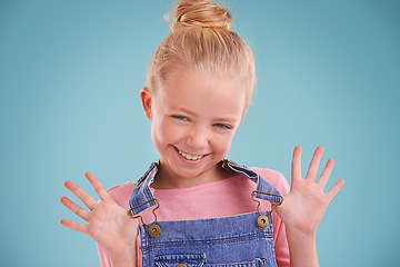 Image showing Child, portrait and happy in studio with confidence in dungarees on blue background, good mood or mockup space. Girl, school student and smile for playful hands or expression, childhood or positivity
