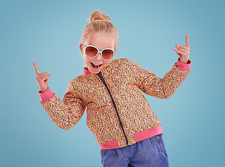 Image showing Happy, sunglasses and portrait of child in studio with funky, trendy and stylish jacket for outfit. Excited, pointing and face of girl kid model with cool fashion and accessory by blue background.