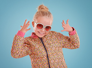 Image showing Little girl, portrait and fashion with sunglasses in studio for trendy, cool and funky style with confidence. Cute child, smile and happy in blue background, young kid and retro clothes with glasses