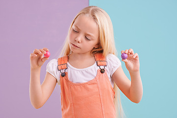 Image showing Studio, girl and decision with candy, dessert and choice for snack and childhood. Child, gumball and yummy selection for tasty, eating and choosing on vibrant split pastel pink and blue background