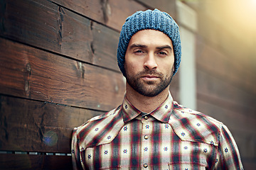 Image showing Portrait, confident and man on wood wall background outdoor in casual clothes, outfit or apparel. Face, serious and stylish person in beanie, shirt and trendy fashion for profile picture in Spain