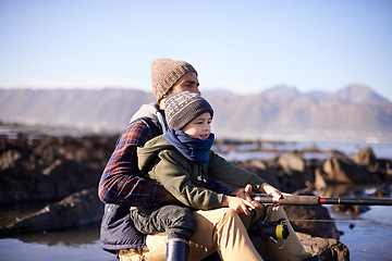 Image showing Father, fishing and young boy on rocks, teaching and bonding for activity by ocean. Sea, rod and learning how to fish for childhood development, winter and hobby together while on seaside vacation