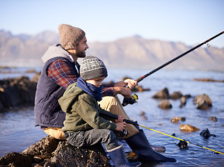 Image showing Father, fishing rod and young boy on rocks, shoreline and bonding for activity by ocean. Sea, catch and learning how to fish for childhood development, winter and hobby while on seaside vacation