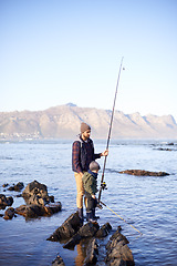 Image showing Father, fishing rod and young boy on rocks, teaching and bonding for activity by ocean. Sea, teach and learn to fish for childhood development, winter and hobby together while on countryside vacation