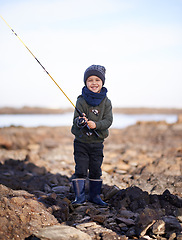 Image showing Portrait, fishing rod and happy boy on shoreline, rocks and smile for activity by ocean. Sea, catch and learning how to fish for childhood development, young child and hobby while on seaside vacation