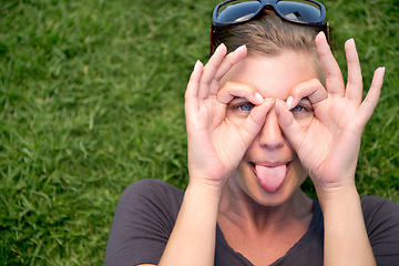 Image showing Portrait, hand glasses and woman with tongue out for funny face, goofy or silly in outdoor garden. Top view, comic and female person joking for humor, finger shape gesture and playful mood in park