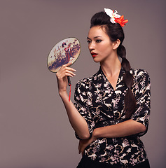 Image showing Japanese woman, fashion and traditional fan with confidence in studio on brown background for culture, style and elegant. Female person, shirt and flower in head with designer clothes or outfit