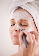 Image showing Hand, mature woman and mask with brush in studio for skincare or anti aging on self care, wellness and fresh skin. Closeup, female person and glow with smile or happy for facial and beauty for luxury