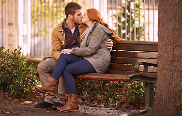 Image showing Couple, love and sitting with kiss at park in cold weather or winter, together and support in London. Relationship, commitment and bonding for romance with soulmate, care and happiness with affection