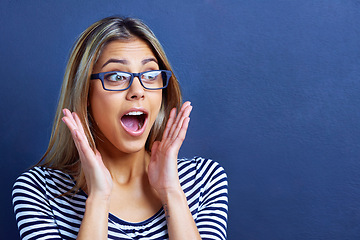 Image showing Studio, scream and woman in shock with hands for promo or deal for clothes in fashion, sale and discount. Adult, female person and girl in blue background with glasses, aesthetic and announcement