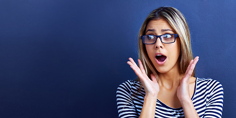 Image showing Studio, news and woman in shock with hands for promo or deal for clothes in fashion, sale and discount. Adult, female person and girl in blue background with glasses, mock up and announcement