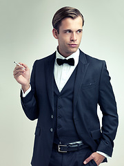 Image showing Elegant, tuxedo or gentleman smoke a cigarette for planning, studio or vintage fashion by white background. Class, confidence or young man for thinking in retro suit, bow tie or idea in formal style
