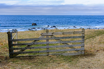 Image showing Weathered wooden fence overlooking rocky shoreline on cloudy day