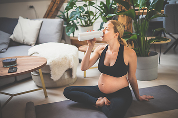 Image showing Young happy and cheerful beautiful pregnant woman taking a break, hydrating, drinking water from the botle after home well being workout program.