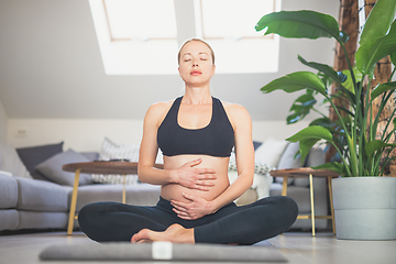 Image showing Young beautiful pregnant woman training yoga, caressing her belly. Young happy expectant relaxing, thinking about her baby and enjoying her future life. Motherhood, pregnancy, yoga concept.