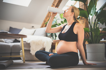 Image showing Young happy and cheerful beautiful pregnant woman taking a break, hydrating, drinking water from the botle after home well being workout progrem.