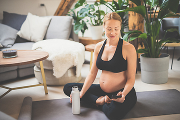 Image showing Young happy and cheerful beautiful pregnant woman chating to family and friends on mobile phone while staying fit, sporty and active on her maternity leave. Pregnancy, yoga concept