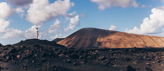 Image showing Woman rising hands up in the sky, enjoying amazing views of volcanic landscape in Timanfaya national park on Lanzarote, Spain. Freedom and travel adventure concept.