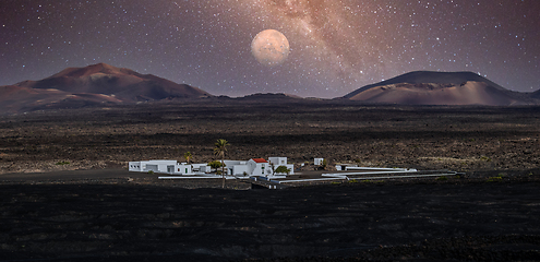 Image showing Amazing nocturnal panoramic landscape of volcano craters in Timanfaya national park. Full moon over La Gueria, Lanzarote island, Canary islans, Spain. Artistic night sky picture